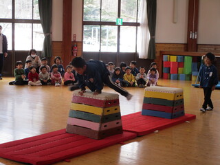 子どもがカラフルな跳び箱を跳んでいるところを沢山の子どもが見ています